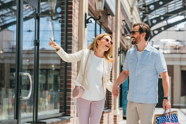 Happy wife pointing on something to husband in shopping mall — Stock Photo