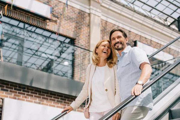 Riéndose pareja adulta en escalera mecánica en centro comercial - foto de stock