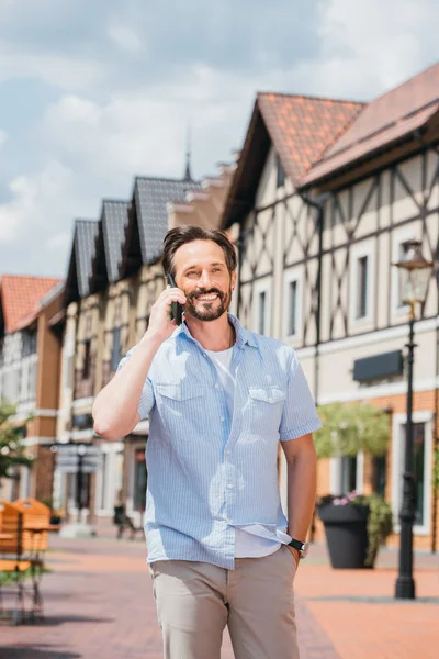 Sonriente hombre guapo hablando por teléfono inteligente en la ciudad - foto de stock