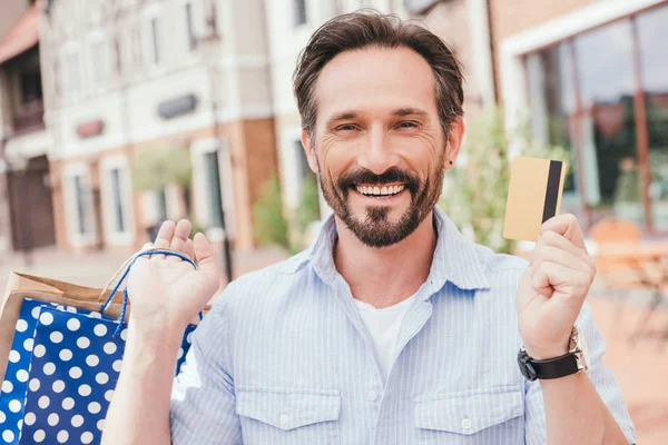 Uomo bello sorridente che tiene la carta di credito e guarda la macchina fotografica — Foto stock