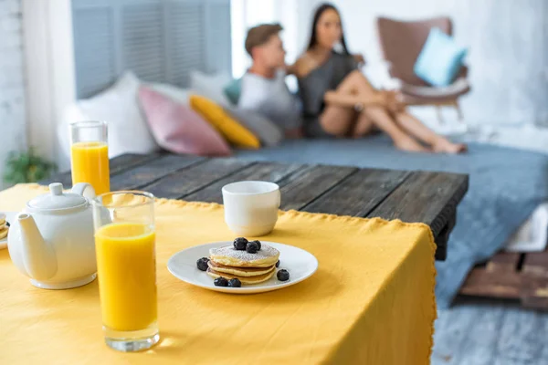 Selektiver Frühstücksfokus auf Tisch und verliebtes Paar, das sich auf dem Bett im Schlafzimmer ausruht — Stockfoto