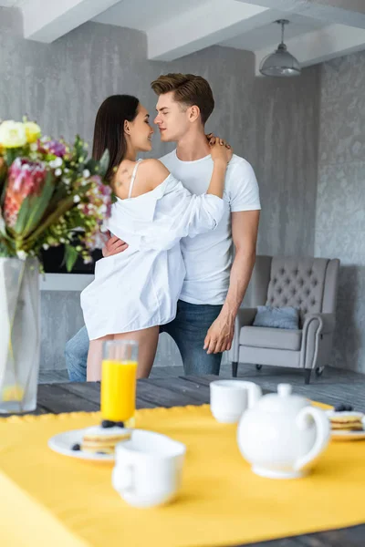 Selective focus of breakfast on table and multiracial couple in love hugging at home — Stock Photo