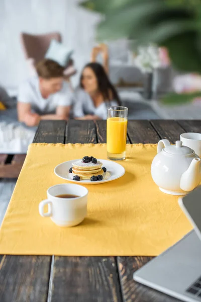 Enfoque selectivo de desayuno en la mesa y pareja en el amor acostado en la cama en el dormitorio - foto de stock