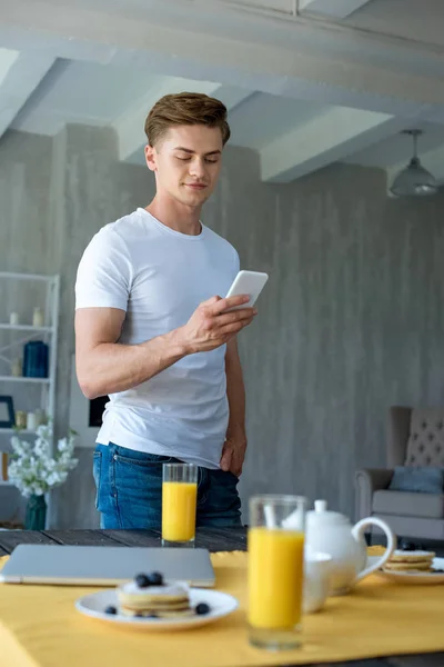 Enfoque selectivo del hombre utilizando el teléfono inteligente y el desayuno en la mesa en casa - foto de stock