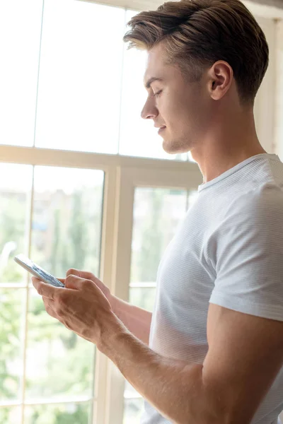 Боковой вид молодого человека, использующего смартфон дома — стоковое фото