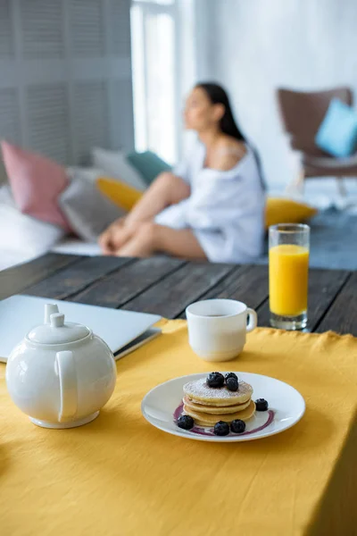 Foyer sélectif du petit déjeuner sur la table et femme asiatique sur le lit dans la chambre — Photo de stock