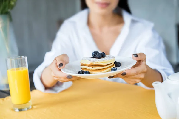 Abgeschnittene Aufnahme einer Frau mit Pfannkuchen serviert mit Blaubeeren auf Teller in den Händen zu Hause — Stockfoto