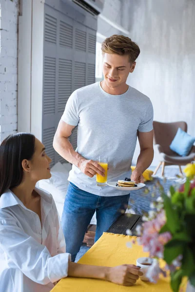 Caucásico hombre trajo desayuno a asiático novia en blanco camisa en mesa en casa - foto de stock
