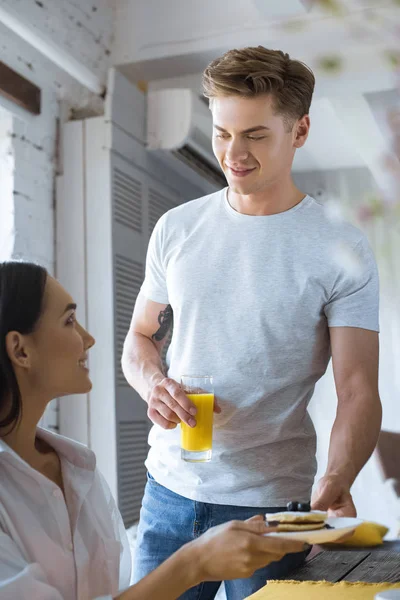 Kaukasischer Mann brachte seiner asiatischen Freundin im weißen Hemd am heimischen Tisch das Frühstück — Stockfoto