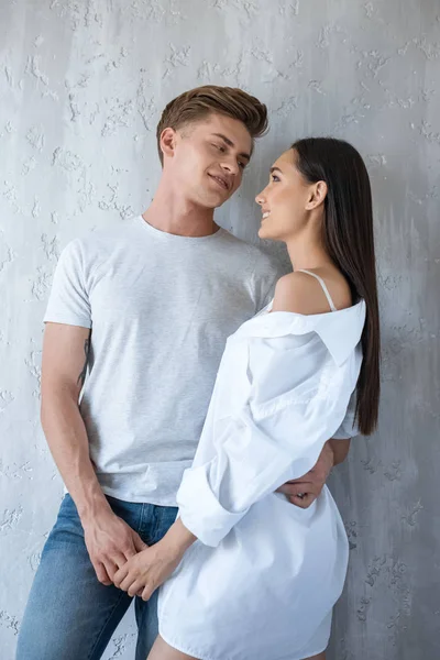 Portrait of smiling interracial couple holding hands and looking at each other at home — Stock Photo