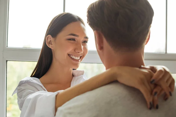 Partial view of smiling asian woman hugging boyfriend at window — Stock Photo