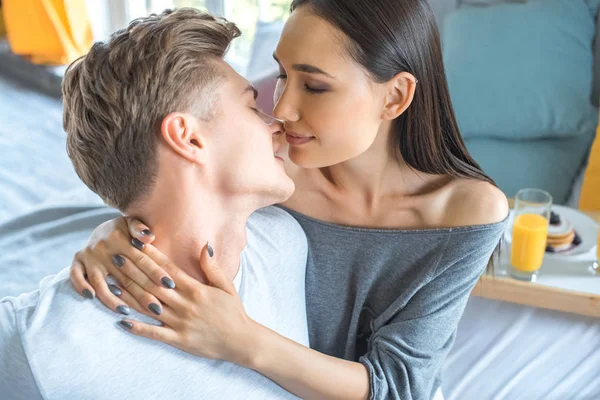 Selektiver Fokus eines verliebten multirassischen Paares mit Frühstück auf einem Holztablett auf dem heimischen Bett — Stockfoto