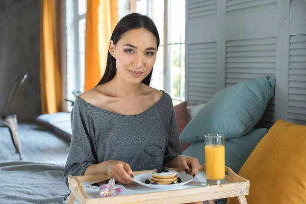 Portrait of smiling asian woman with breakfast on wooden tray in bedroom — Stock Photo