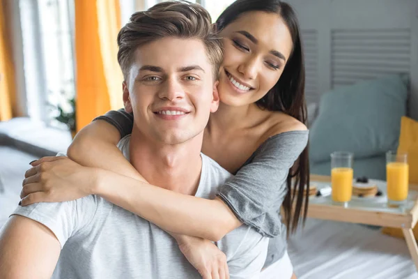 Selective focus of multiracial couple in love and breakfast on wooden tray on bed at home — Stock Photo