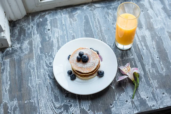 Close up view of glass of juice and homemade pancakes for breakfast on wooden surface — Stock Photo