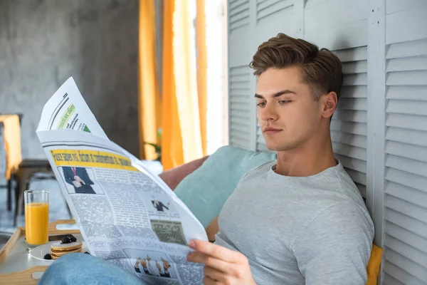 Visão lateral do jovem lendo jornal na cama de manhã — Fotografia de Stock