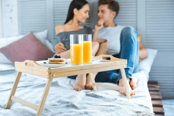 Selective focus of multicultural couple and breakfast on wooden tray on bed in bedroom — Stock Photo