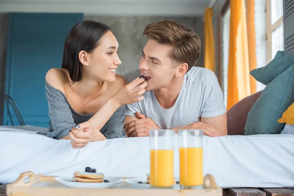 Portrait of asian woman feeding caucasian boyfriend with breakfast in bed at home — Stock Photo