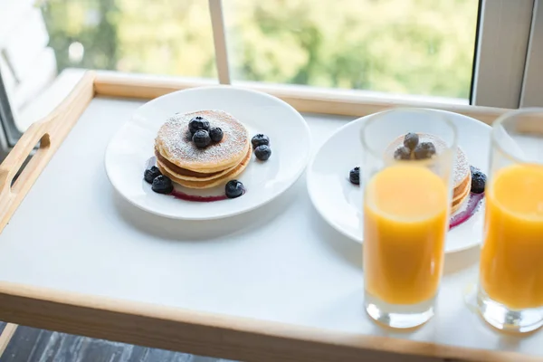 Primer plano vista del vaso de jugo y panqueques para el desayuno en bandeja de madera - foto de stock