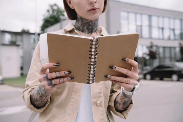 Imagen recortada de mujer tatuada leyendo libro de texto en la calle - foto de stock