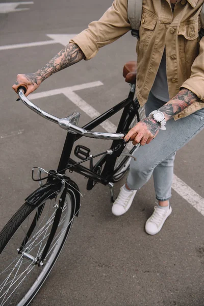Частичный вид женщины с татуировкой, стоящей с велосипедом на парковке — стоковое фото