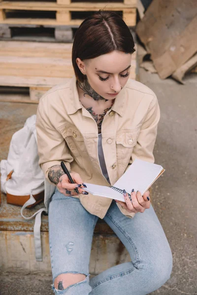 Vista ad alto angolo di elegante donna tatuata seduta con libro di testo vuoto — Foto stock