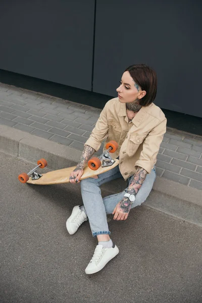 Vista ad alto angolo di donna elegante seduta con skateboard in strada — Foto stock