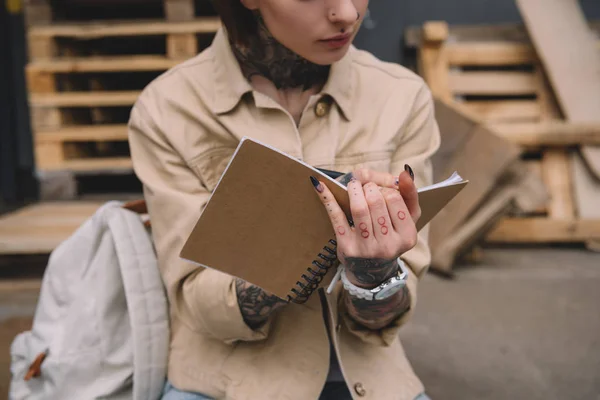 Cropped image of tattooed woman writing in textbook — Stock Photo