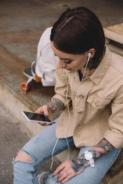 High angle view of stylish tattooed woman in earphones listening music with smartphone — Stock Photo