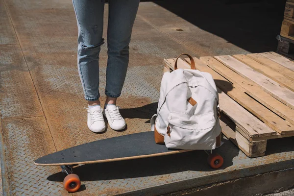 Imagem cortada de mulher de pé perto de mochila e skate — Fotografia de Stock