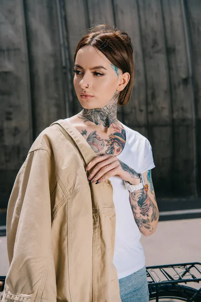 Porträt einer tätowierten Frau mit Jacke auf der Schulter, die wegschaut — Stockfoto