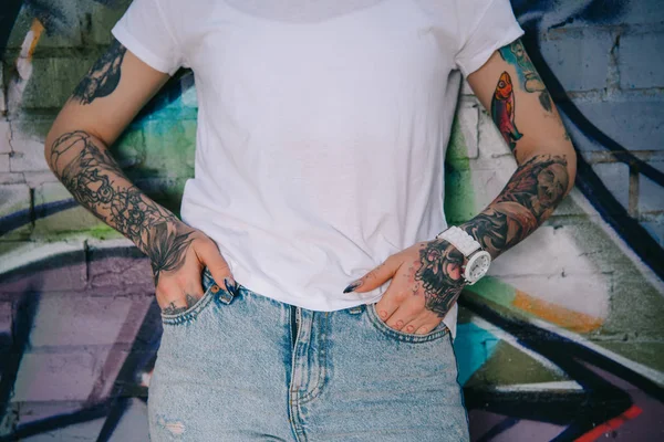 Cropped image of tattooed woman standing against wall with colorful graffiti — Stock Photo