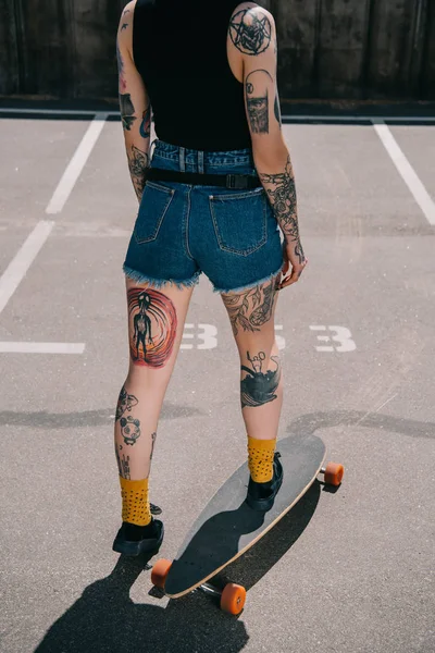Cropped image of stylish tattooed girl skateboarding at parking lot — Stock Photo