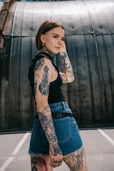Attraente ragazza con tatuaggi guardando lontano e posa in strada — Foto stock