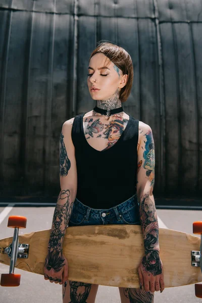 Atraente elegante tatuado menina com olhos fechados segurando skate — Fotografia de Stock