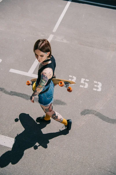 Vista aérea de la joven mujer tatuada sosteniendo monopatín en el estacionamiento — Stock Photo