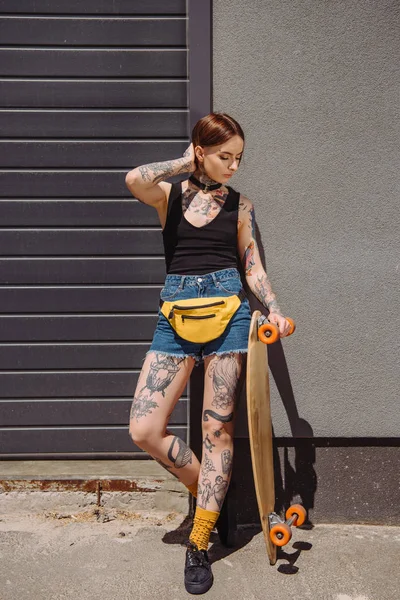 Attractive stylish tattooed girl standing with skateboard at street — Stock Photo