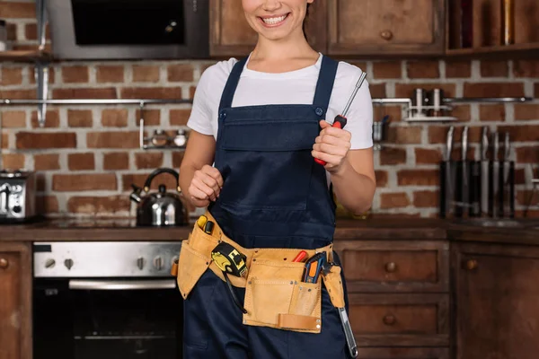 Обрезанный снимок улыбающейся молодой ремонтницы с отвёрткой, стоящей на кухне — стоковое фото
