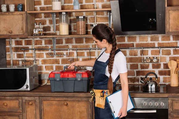 Young repairwoman with toolbox and clipboard standing at kitchen — Stock Photo