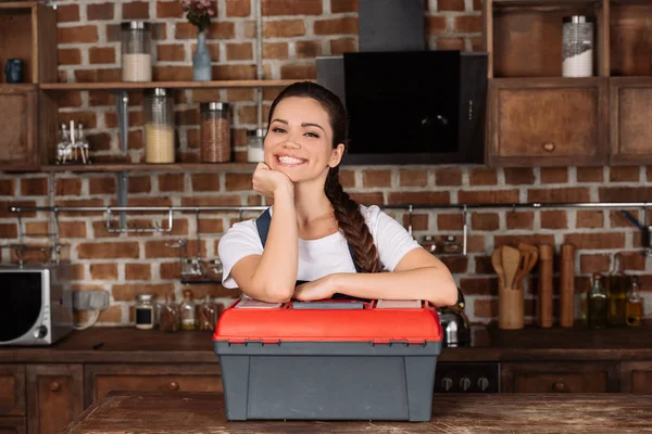 Lächelnde junge Reparaturfrau lehnt an Werkzeugkiste und blickt in die Kamera — Stockfoto