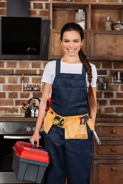 Belle jeune réparatrice avec des outils debout à la cuisine et regardant la caméra — Photo de stock