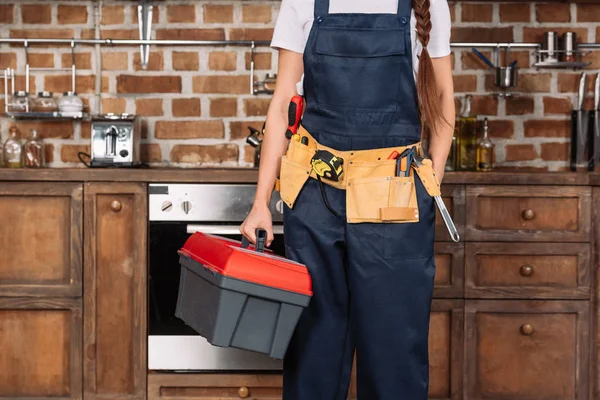 Tiro recortado de reparadora con caja de herramientas y cinturón de herramientas de pie en la cocina - foto de stock