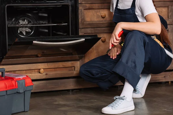 Abgeschnittene Aufnahme einer Reparaturfrau mit einer Zange, die in der Nähe des Ofens sitzt — Stockfoto