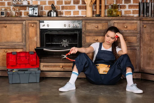 Cansada joven reparadora sentada en el suelo en la cocina - foto de stock