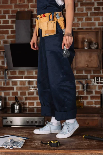 Ritagliato colpo di riparatore con lampadina e strumenti in piedi sul tavolo della cucina — Foto stock