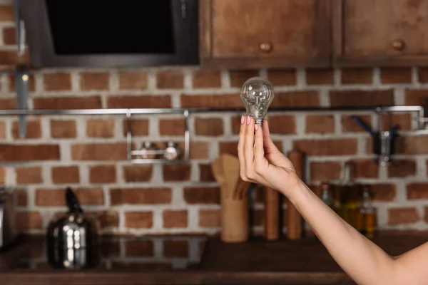 Cropped shot of woman holding light bulb at kitchen — Stock Photo
