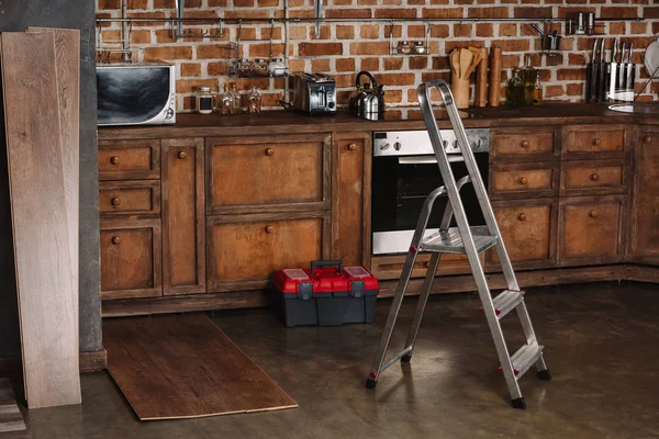 Interior de la cocina estilo loft con escalera, caja de herramientas y tablones laminados en el suelo - foto de stock