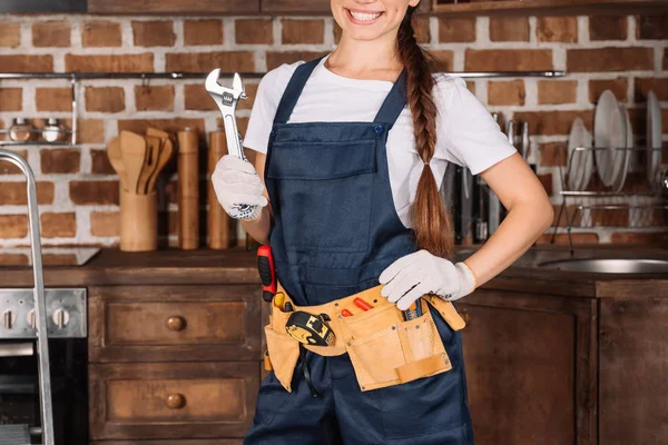 Recortado disparo de sonriente joven reparadora con cinturón de herramientas y llave inglesa - foto de stock