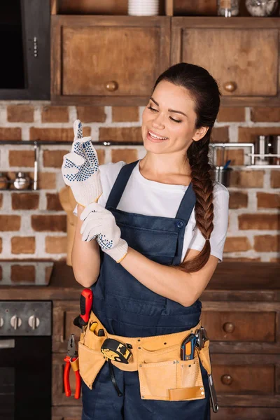 Happy young repairwoman putting on work gloves at kitchen — Stock Photo