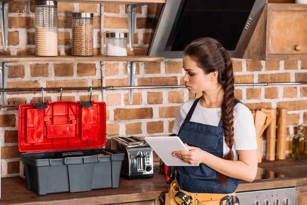 Seria giovane riparatrice con cassetta degli attrezzi utilizzando tablet in cucina — Foto stock